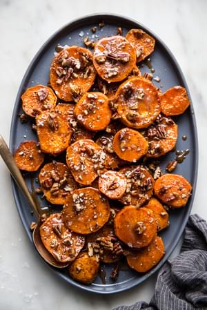 sliced Candied Yams with Honey, Brown Sugar and pecans on a platter with a serving spoon