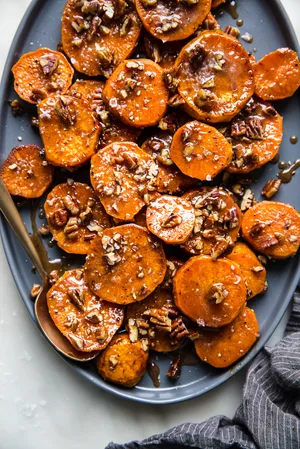 sliced and roasted Candied Yams with Honey, Brown Sugar and pecans on a platter with a serving spoon