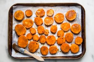 slices of sweet potatoes brushed with brown sugar and honey sauce on a parchment paper lined sheet pan