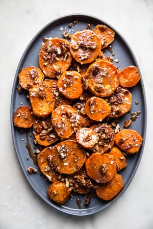 sliced candied yams with Honey and Brown Sugar and pecans on a platter with a serving spoon