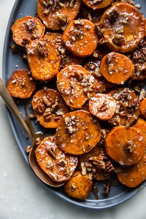 sliced Candied sweet potatoes with Honey, Brown Sugar and pecans on a platter with a serving spoon