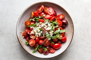 marinated tomato salad ingredients cherry tomatoes, balsamic, salt and garlic, lemon, basil, pepper and olive oil in a bowl