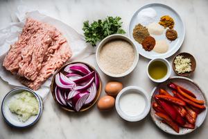 ingredients for chicken meatballs including ground chicken, red onions, bread crumbs, eggs, bell peppers, onions and spices.