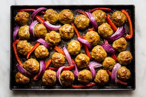 Baked chicken shawarma meatballs shown on a baking sheet with bell peppers and red onions.