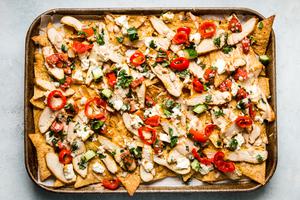 chicken shawarma nachos on a sheet pan topped with pepadews, cucumber, fresh parsley and lemon juice