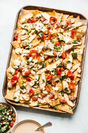 chicken shawarma nachos shown next to a bowl of tahini sauce and Mediterranean salsa