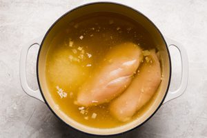 chicken breast and rice cooking in a pot of chicken stock with onion and garlic to make chicken and rice soup