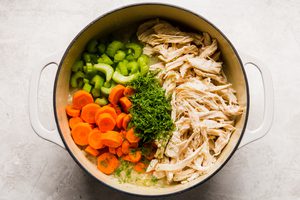 shredded chicken, carrots, dill, celery being added to a pot of homemade chicken a rice soup