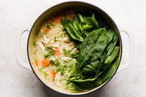 spinach being added to homemade chicken and rice soup cooking in a pot