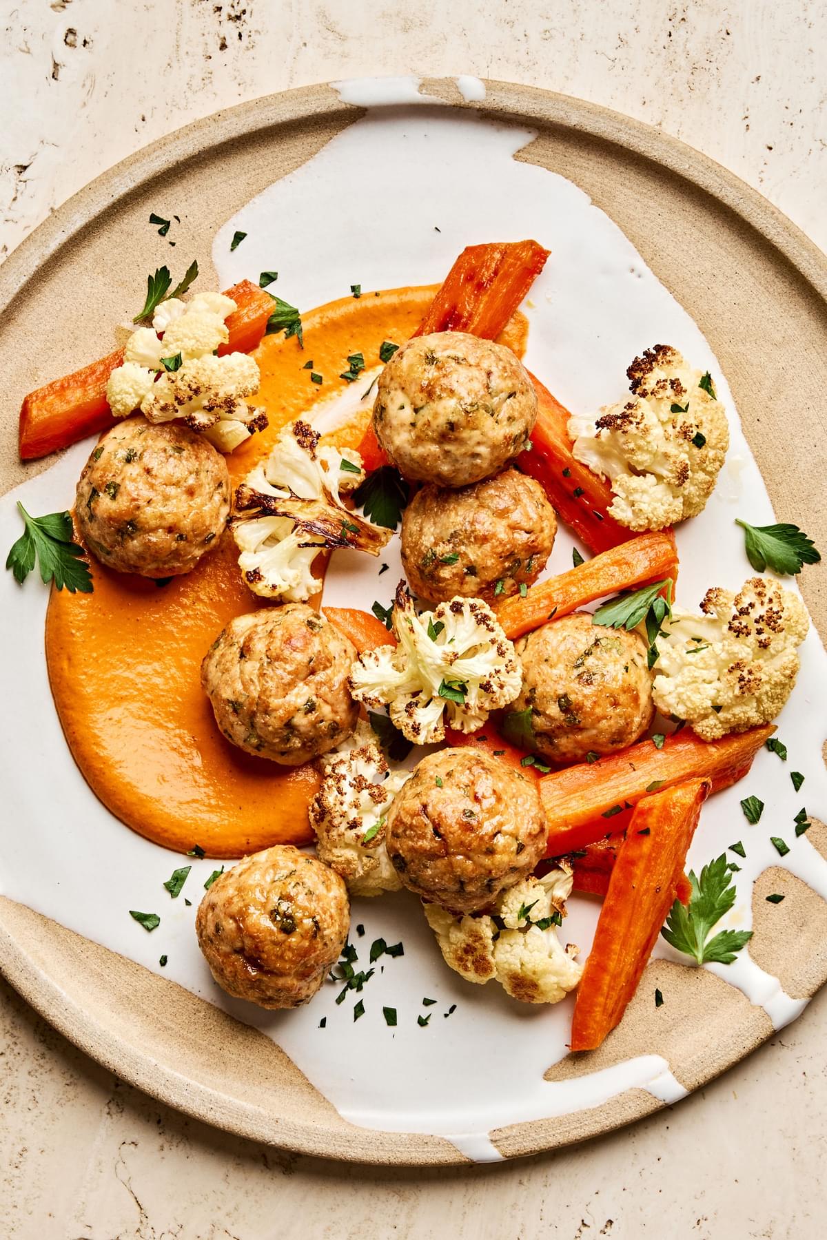 Romesco sauce on a plate piled with Chicken meatballs and roasted carrots and cauliflower that were all baked on a sheet pan
