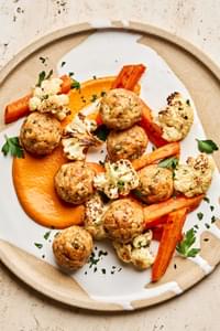 Romesco sauce on a plate piled with Chicken meatballs and roasted carrots and cauliflower that were all baked on a sheet pan
