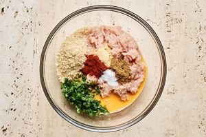 raw ingredients in a mixing bowl for chicken meatballs, including ground chicken, breadcrumbs, egg, parsley & spices
