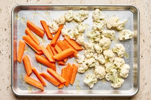 raw, chopped carrots and cauliflower being tossed with olive oil and salt on a baking sheet