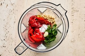 Top-down view of ingredients in a blender to make Romesco sauce: roasted red peppers, nuts, and spices