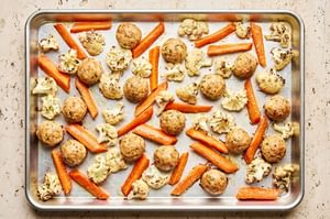 baked Chicken meatballs and roasted carrots and cauliflower arranged on a sheet pan hot out of the oven