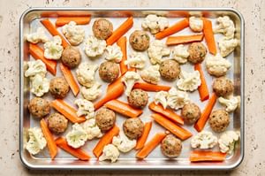 Chicken meatballs and carrots and cauliflower arranged on a sheet pan ready to be roasted in the oven