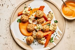 Romesco sauce on a plate piled with chicken meatballs and roasted carrots and cauliflower that were all baked on a sheet pan