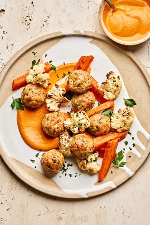 Romesco sauce on a plate piled with chicken meatballs and roasted carrots and cauliflower that were all baked on a sheet pan