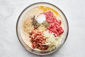 Ground beef, breadcrumbs, onions, eggs, and spices being mixed together in a bowl to create a flavorful meatloaf mixture.