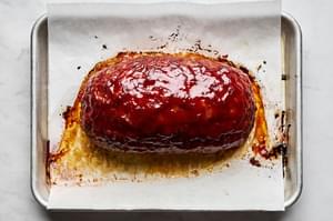 Golden-brown meatloaf on a parchment-lined baking sheet, freshly out of the oven, ready to be sliced and served.