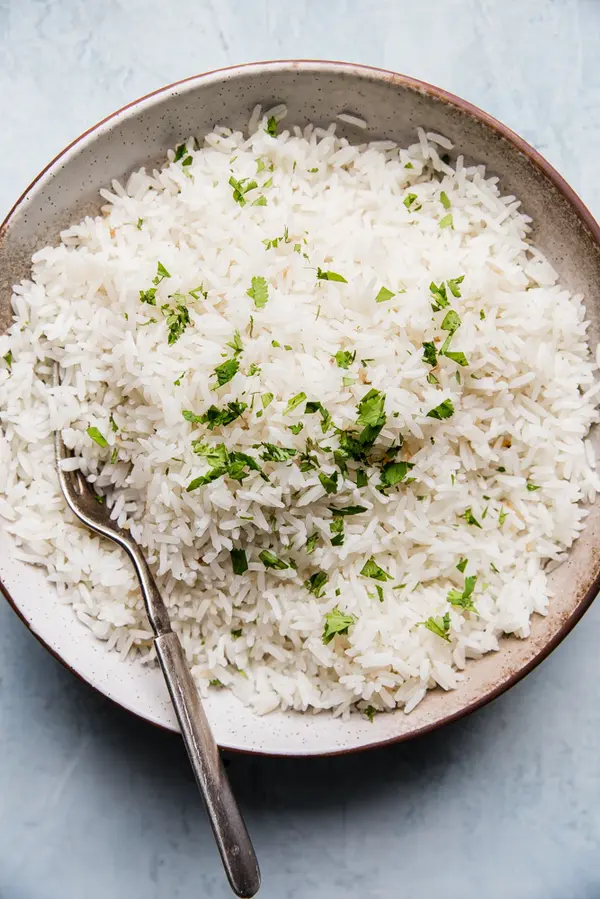 A bowl of creamy coconut rice made with coconut milk, salt, and sugar, garnished with a touch of cilantro