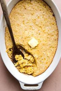 homemade Spoon bread made with creamed corn and butter being scooped out of a casserole dish