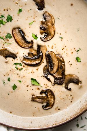 a pot of homemade cream of mushroom soup with heavy cream parsley, onions and garlic in a bowl