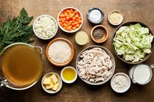 Ingredients laid out for creamy chicken and rice soup: shredded chicken, chopped veggies, butter, flour, spices broth & milk