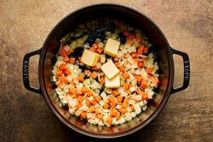 Butter added to a pot with onion, carrot, and garlic cooking in olive oil.