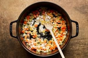 Flour being stirred into carrot, onion, garlic and butter in a pot.