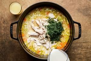 A pot of creamy chicken and rice soup being stirred, with milk, dill, lemon juice, and tender shredded chicken.