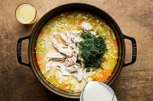 A pot of creamy chicken and rice soup being stirred, with milk, dill, lemon juice, and tender shredded chicken.