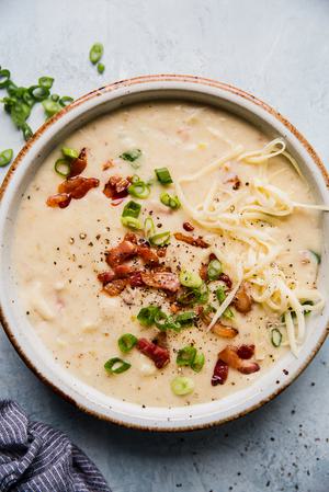 a bowl of creamy potato soup made with bacon, leeks and cream topped with extra bacon green onions and white cheddar cheese