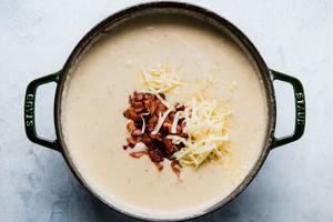 bacon and shredded white cheddar being added to a pot of homemade creamy potato soup
