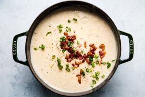 a pot of creamy potato soup made with bacon, leeks and cream topped with extra bacon green onions and white cheddar cheese