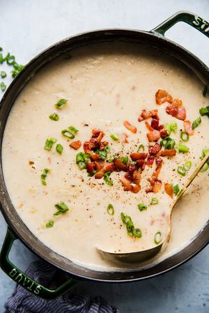 a pot of creamy potato soup made with bacon, leeks and cream topped with extra bacon green onions and white cheddar cheese