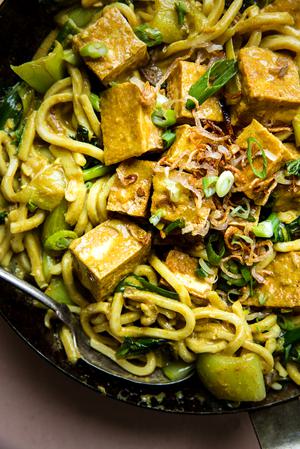 Crispy Tofu with Creamy Curry Udon Noodles in a sauce pan with fried shallots, baby bok choy, and green onions