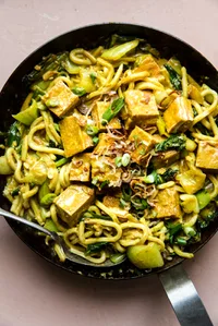 crispy tofu with creamy curry udon noodles in a saucepan with a serving spoon