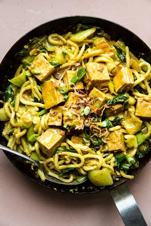 crispy tofu with creamy curry udon noodles in a saucepan with a serving spoon