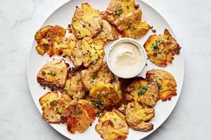 a plate of crispy smashed potatoes seasoned with salt and garlic sprinkled with chives and served with garlic aioli