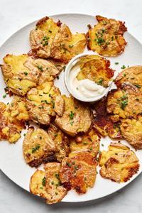 a plate of crispy smashed potatoes seasoned with salt and garlic sprinkled with chives and served with garlic aioli