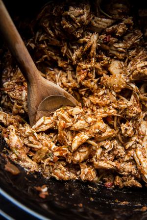 crock pot chicken taco meat shown shredded in a crockpot with a wooden spoon