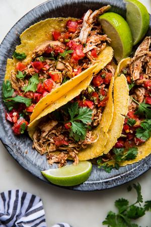three tacos in a blue metal pan shown with limes and fresh salsa