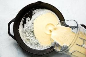 batter for dutch baby pancake being poured into a hot cast iron skillet with butter
