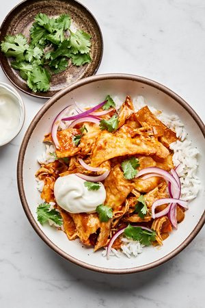 Skillet chicken enchiladas served on top of rice topped with cilantro, sour cream and red onions, a delicious mexican dinner