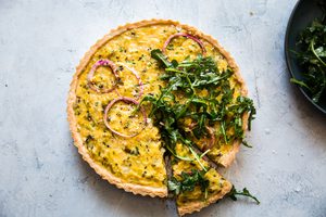 A Five Onion Tart topped with arugula salad in a list of delicious breakfast recipes