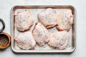 chicken thighs patted dry being seasoned with salt and pepper on a baking sheet
