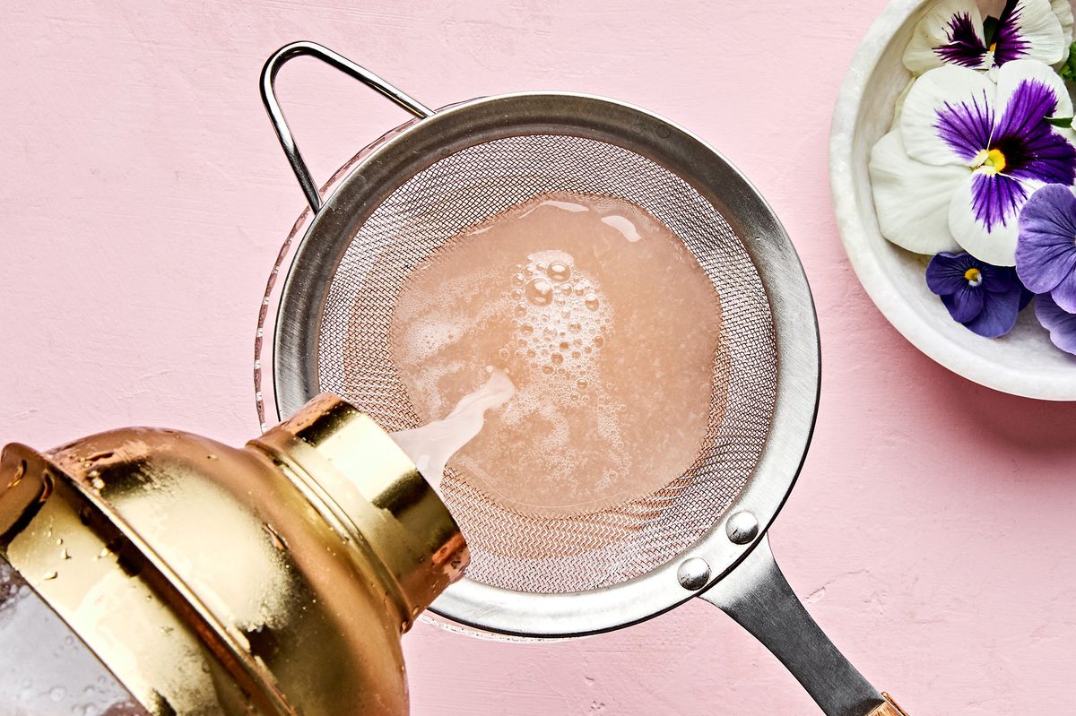 ingredients for a Grapefruit Pisco Sour with Orange Bitters being being strained into a cocktail glass