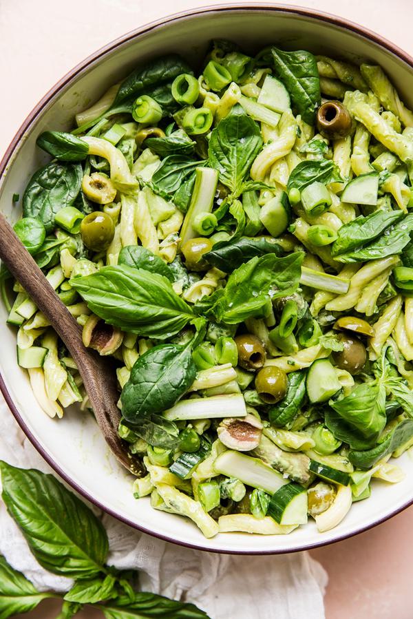 Green goddess pasta salad with basil, green olives, asparagus, snap peas and cucumbers in a a bowl with a wooden spoon