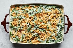 grean beans tossed in cream sauce and topped with french fried onions in a casserole dish ready to be baked in the oven